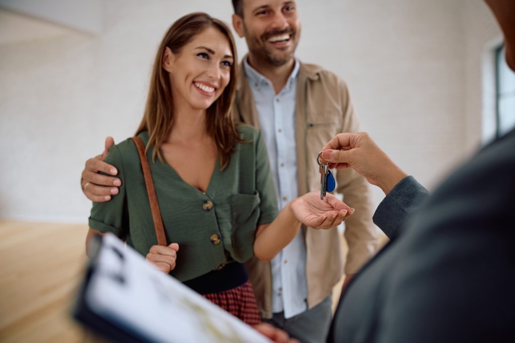 Happy woman and her husband getting keys from real estate agent while buying a new apartment.